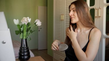 Gülümseyen esmer kadın makyaj masasında oturuyor ve uzun saçlarını tarıyor. Saç bakımı, kadın zarafeti ve güzelliği.