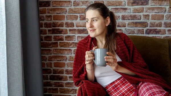 一个微笑的女人躺在沙发上 躺在茶杯下 望着窗外的画像 妇女在家休息 生活方式和放松 — 图库照片