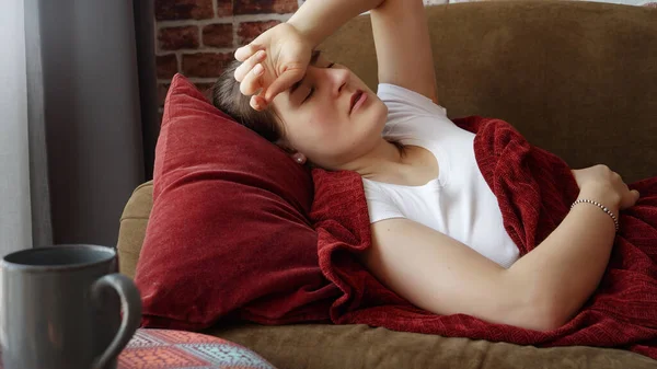 Młoda Chora Kobieta Bólem Głowy Leżąca Kanapie Trzymająca Się Rękę — Zdjęcie stockowe
