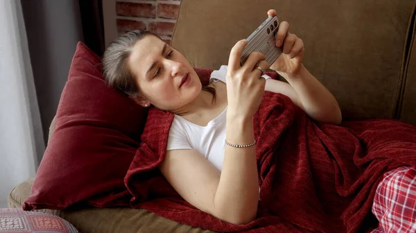 Молодая Улыбающаяся Женщина Лежит Диване Играет Видеоигры Смартфоне Развлечения Дома — стоковое фото