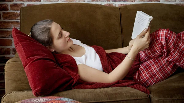パジャマ姿の若い女性がソファに横になって本を読んでいる姿 女性のレジャーで休んでいる人々 — ストック写真