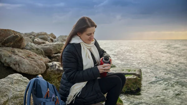 在寒冷多风的天气里 坐在美丽的海岸线上 一头长发的女人正享受着一杯热茶 很好用于度假和旅行视频 — 图库照片