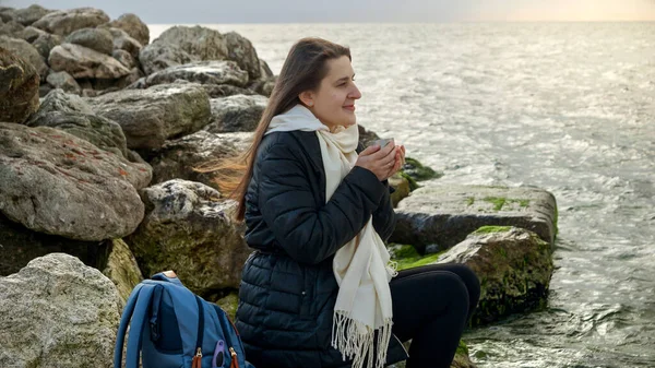 年轻的女人留着长发 一边喝着热茶 一边欣赏着汹涌的海滨美景 最适合用于度假或度假视频 — 图库照片