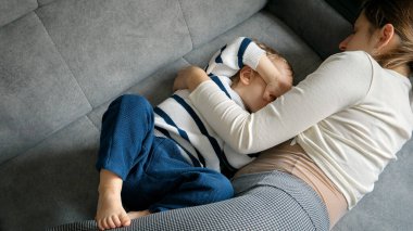 Genç anne küçük oğluyla kanepede yatar ve onu anne sütüyle besler. Emzirme kavramı, çocuk gelişimi, doğal beslenme