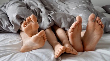 Aile sevgisini, sıcaklığı ve birlikteliği temsil eden battaniyenin altında ebeveynlerin ve çocuklarının ayaklarının yakın çekimi.