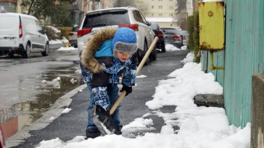 Küçük çocuk karla kaplı arka bahçeyi kürekle temizliyor. Kış, kar temizleme ve çocuk gelişimi.