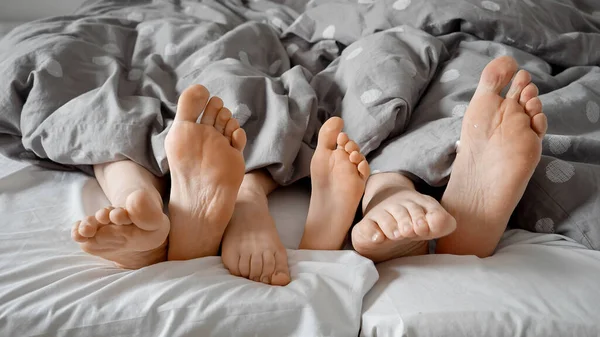 Parent\'s and child\'s feet happily tapping and wiggling under the blanket on a comfortable bed. Concept of family love, bonding, and playful moments shared at home