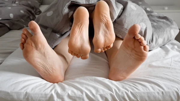Loving couple\'s feet having sex, an intimate moment under the blanket on a soft bed. Perfect for showcasing the importance of love and affection in a family.