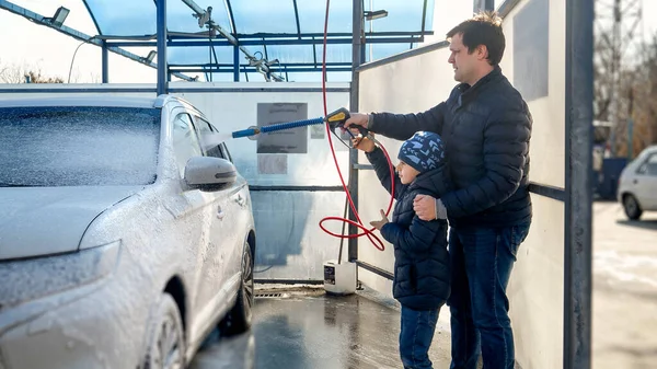 Young father with son washing car at self washing service. Concept of parenting, children helping parents and automobile care