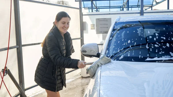 Young woman washing car with shampoo foam and brush. Automobile care, transport cleaning, dirty car