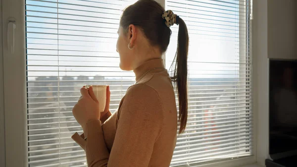 美しい女性はコーヒーを飲み 窓のブラインドを開ける 朝の人 美しい街並み オフィスで休憩している人 — ストック写真