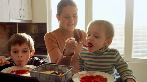 母親と一緒に2人の小さな男の子は 日没の光線でキッチンでホットスープを食べています 家庭料理 家庭料理 子供の健康的な栄養 — ストック写真