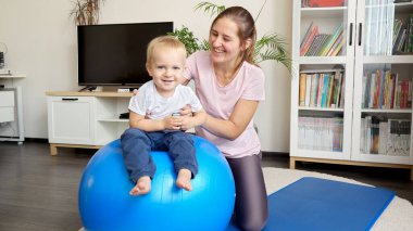 Mutlu gülümseyen bebek annesiyle fitbol oynuyor. Sağlık, spor, yoga ve çocuk gelişimi kavramı.