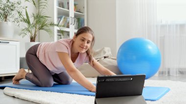 Mutlu gülümseyen kadın tablet bilgisayarda fitness dersi izlerken online spor antrenmanlarına el sallıyor. Evde sağlık, spor ve yoga kavramı