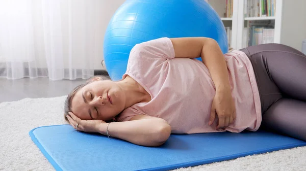 Tired and exhausted woman lying on fitness mat and resting after having intensive fitness training at home