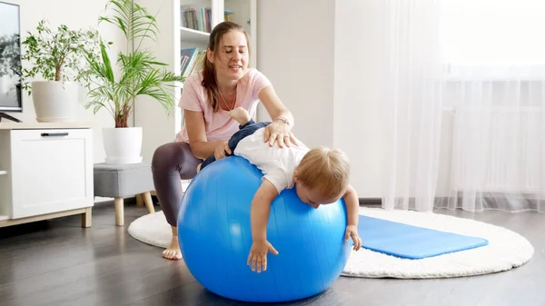 有爱心的年轻母亲伸展她的小儿子的肌肉和在健身球上锻炼 — 图库照片