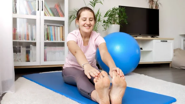 快乐的笑着的女人 双腿伸展着 在健身垫上锻炼时达到了她的脚趾 家庭保健 体育和瑜伽的概念 — 图库照片