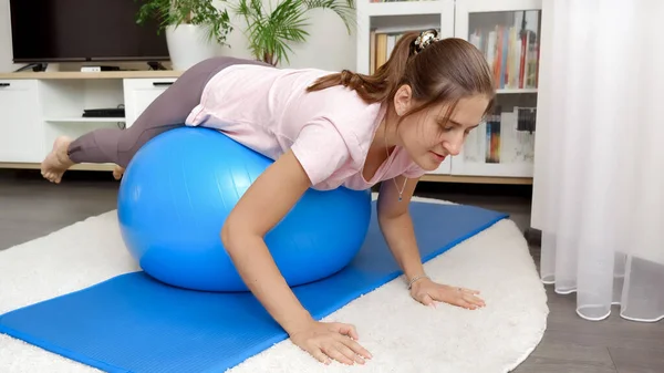 漂亮的黑发女人在家里做健身锻炼 同时在蓝色的大球上打滚 — 图库照片
