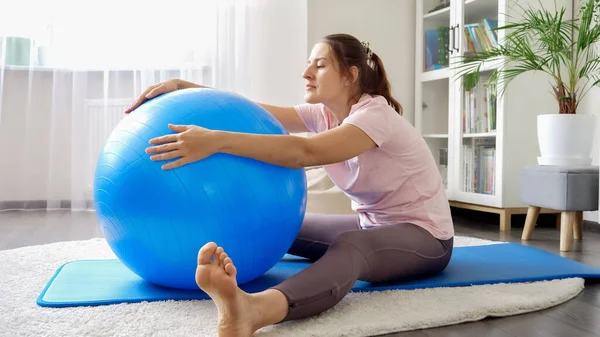 漂亮的年轻女子坐在健身垫上 用适形球做伸展运动 家庭保健 体育和瑜伽的概念 — 图库照片