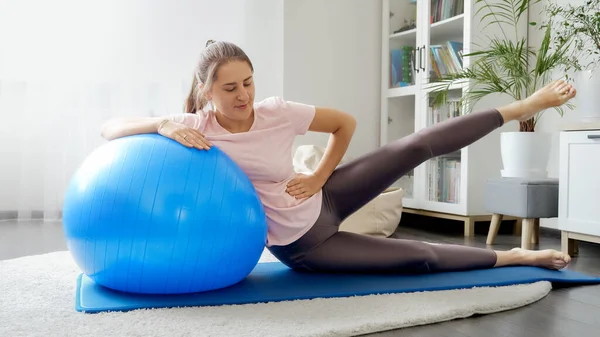 笑着坐在健身垫上的年轻女子与适形球和训练她的腿 家庭保健 体育和瑜伽的概念 — 图库照片