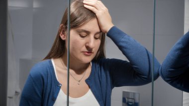 Üzgün kadın banyoda dikiliyor ve aynaya yaslanıyor. Depresyon, stres, zihinsel hastalık ve sorunlar, yalnızlık ve hüsran kavramı