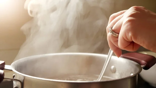 用勺子搅拌金属锅中的女性手煮汤 从热水中慢慢升起的蒸汽 — 图库照片