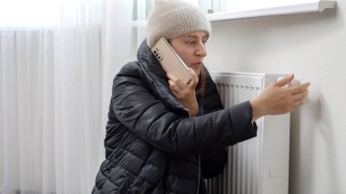 Genç bir kadın evde üşüyormuş. Kaloriferi tamir etmesi için tamirci çağırıyormuş. Enerji krizi, yüksek faturalar, bozuk ısıtma sistemi, ekonomi ve aylık kamu hizmetleri ödemelerinde tasarruf kavramı.