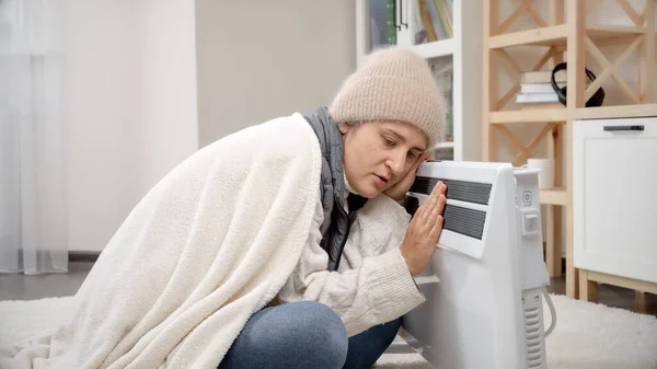 穿着冬衣的年轻女人坐在家里 在电热器里取暖 — 图库照片