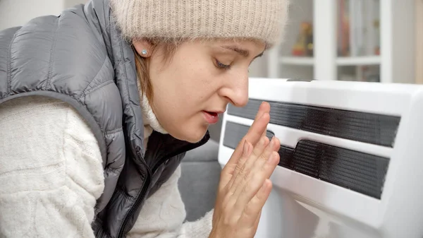 戴帽子的女人在冷藏室的电暖炉前暖手 能源危机的概念 高额费用 经济和节省每月公用事业付款 — 图库照片