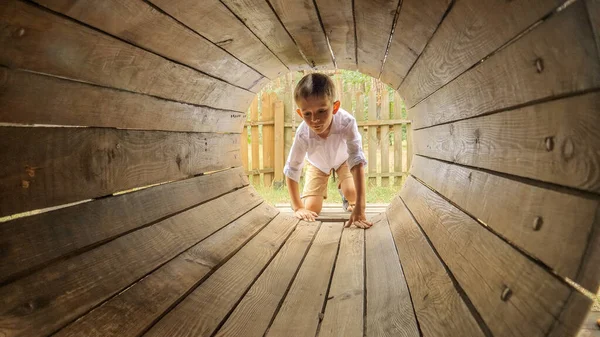 小さな男の子が遊び場の木製のトンネルやパイプを這っています 屋外で遊んでいる子供たち 楽しい夏休みと休日を持っている子供たち — ストック写真