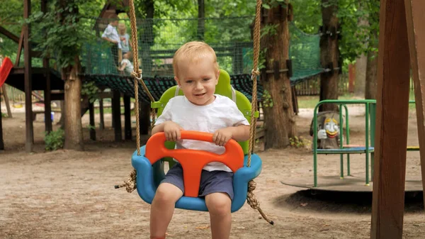 Glücklich Lächelnder Kleiner Junge Schaukelt Auf Dem Spielplatz Bunter Schaukel — Stockfoto