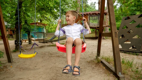 公園の遊び場でスイングしながら楽しんでいる幸せな笑う少年 — ストック写真