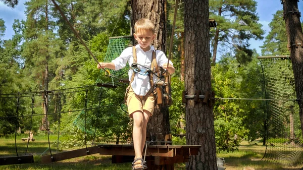 アクティブな少年が公園のロープブリッジを登ったり歩いたり — ストック写真