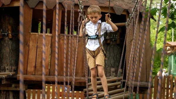 小さな男の子は安全ロープを保持し 夏のキャンプでぐらつき橋を渡ります キッズスポーツ 夏休み 屋外での楽しい スカウト — ストック写真