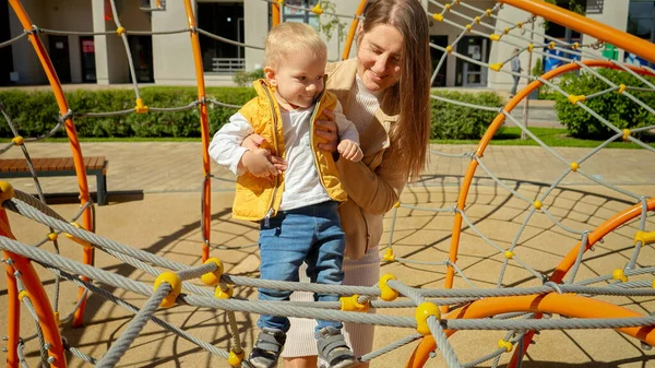 Młoda Opiekuńcza Matka Pomaga Synowi Wspiąć Się Linę Placu Zabaw — Zdjęcie stockowe