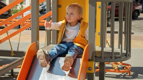 Kleiner Kleinkind Junge Sitzt Auf Der Rutsche Auf Spielplatz Und — Stockfoto