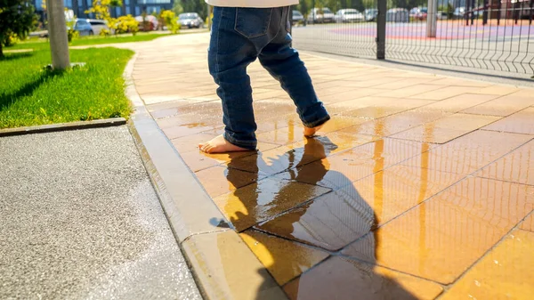 公園や遊び場の道のウェットウォータープードルの上を歩く裸足の幼児のクローズアップ — ストック写真