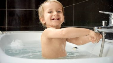 Neşeli erkek bebek banyoda harika vakit geçiriyor ve bulaşıkları yıkıyor. Banyo zamanı bir bebeğin hijyen rutininin önemli bir parçasıdır.