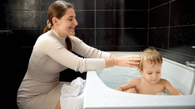 Mutlu gülümseyen anne, bebeğinin evde banyo yapmasını ve dinlenmesini seyrediyor. Ebeveynlik, mutluluk ve çocuk hijyeni kavramı