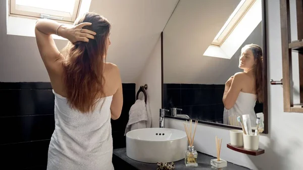Mladá Žena Dlouhými Vlasy Pokryté Ručníkem Koupeli Stojí Zrcadle Dívá — Stock fotografie