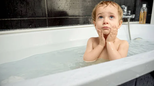 Little baby boy rubbing eyes after splashing water in bath. Child hygiene, fun, playing at home