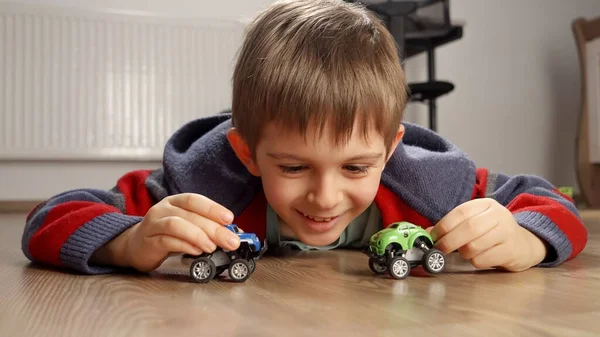 Portret Uroczego Uśmiechniętego Chłopca Leżącego Podłodze Bawiącego Się Zabawkami Samochodowymi — Zdjęcie stockowe
