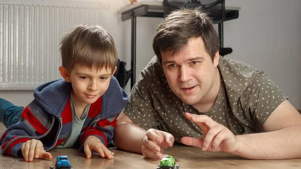 Young father and boy having toy car race on floor in bedroom. Children playing alone, development and education, games at home