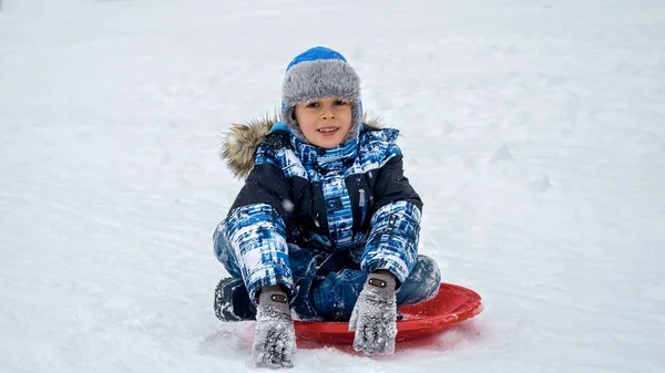 Mutlu Çocuk Portresi Plastik Kızakların Üzerinde Oturuyor Kar Yağarken Kameraya — Stok fotoğraf