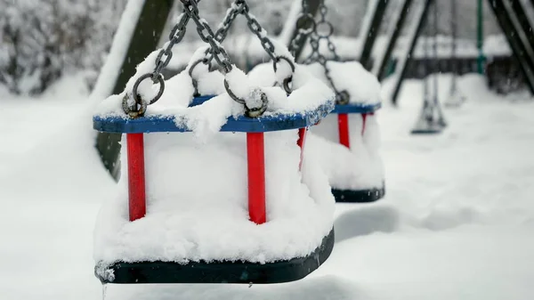 雪花飘落在公共游乐场的空荡荡的秋千上 覆盖着公园的积雪 坏天气和暴风雪的概念 — 图库照片