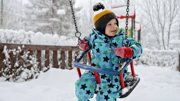 在一个冬季公园里 一个被雪覆盖的操场秋千上 男孩笑着荡秋千 户外运动和寒假的概念 — 图库照片