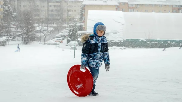 快乐微笑的男孩背着塑料雪橇爬山 然后在下雪天滑倒 寒假快乐有趣 孩子们在户外玩耍 在雪地里活动 — 图库照片