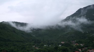 Yüksek dağlardaki küçük köy ağaçlarla kaplanmış ve alçak yağmur bulutlarıyla kaplanmış..