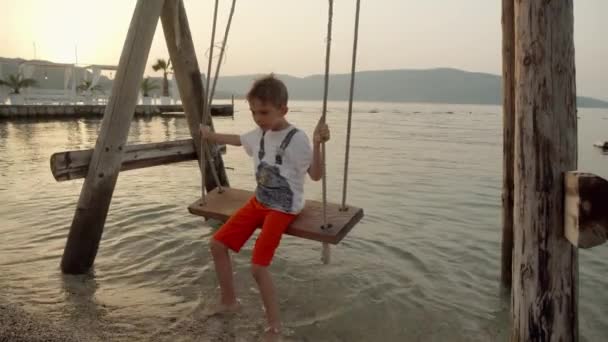 海のビーチでスウィングを楽しんでいる小さな少年 夏休み 観光について — ストック動画