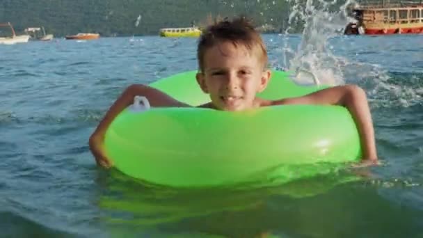 海で膨脹可能なリングで泳いでいる間 幸せな陽気な少年が水を飛ばします 家族の休日 夏時間 — ストック動画